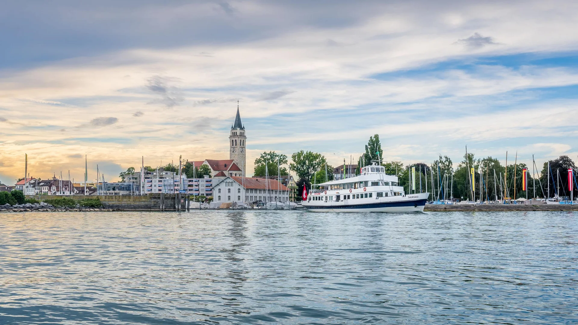 Veerboot op kalm meer met kerk en zeilboten op de achtergrond