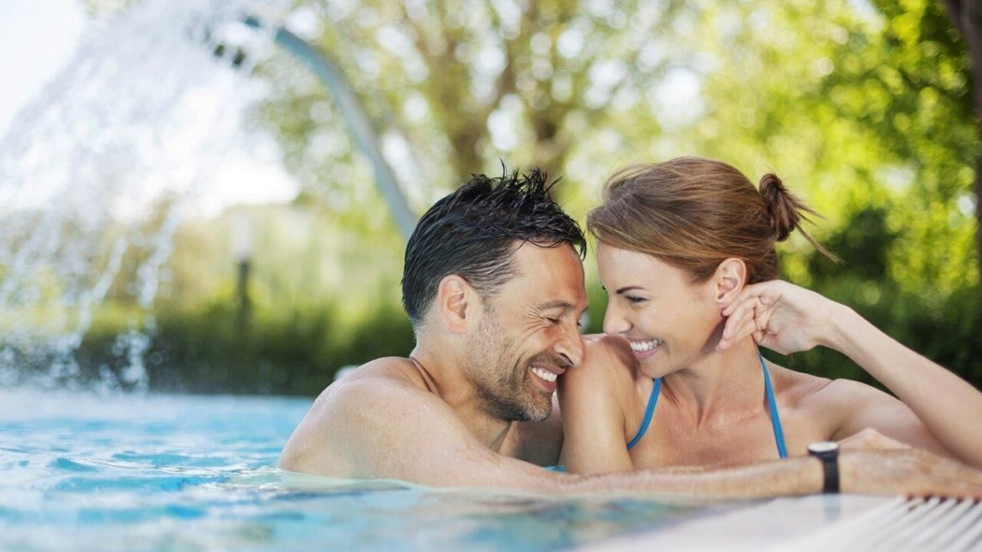 Couple smiling together at pool edge with waterfall in background