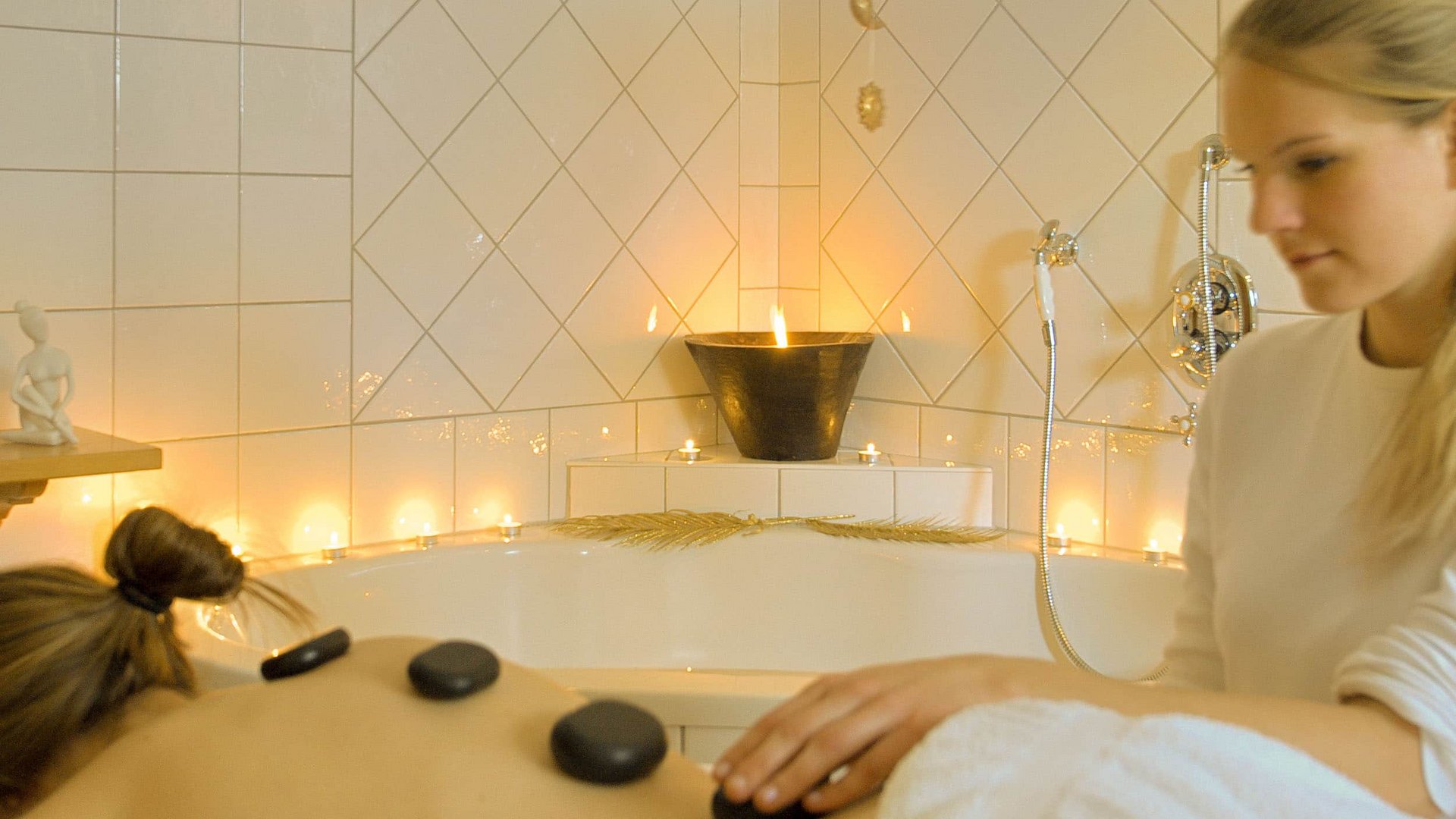 Woman receiving hot stone massage in candlelit spa room