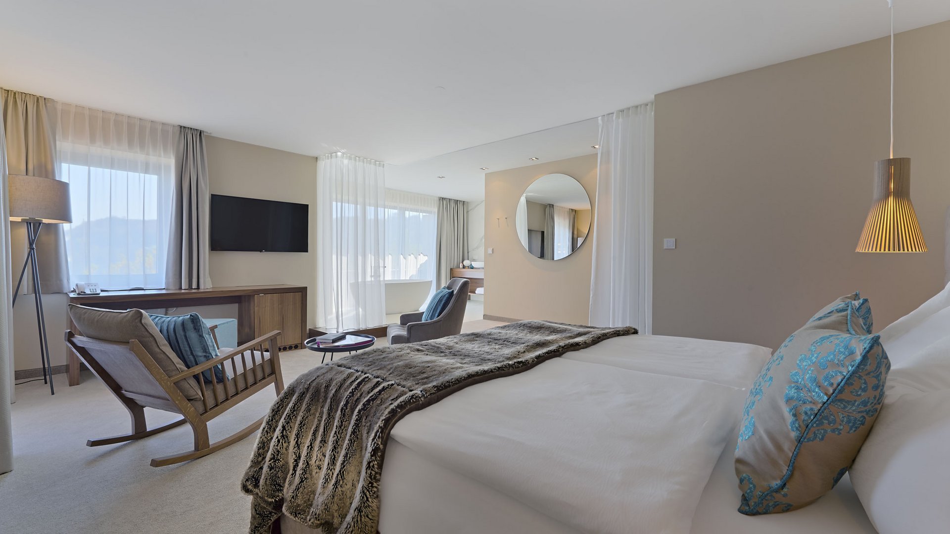 Modern hotel room with bed, armchairs, and large round mirror