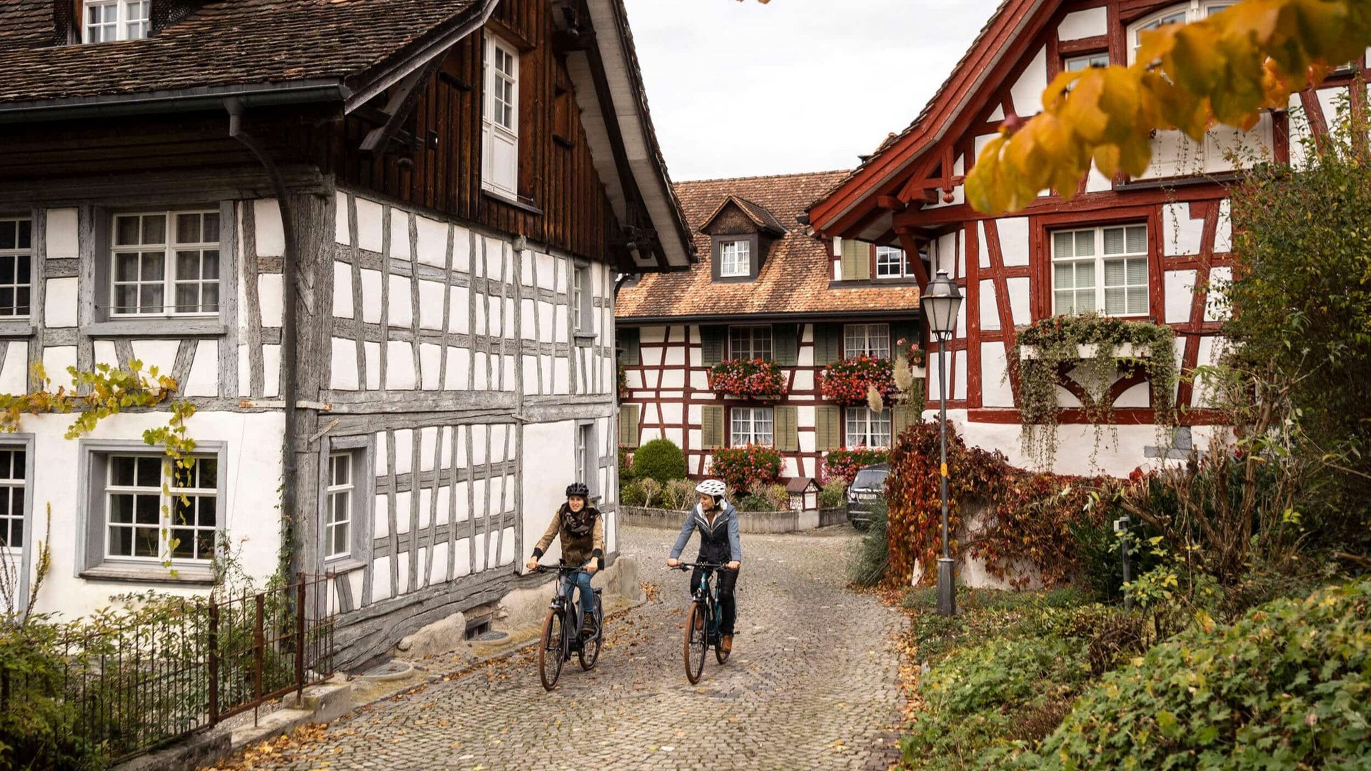 Two cyclists riding through a historic half-timbered village in autumn