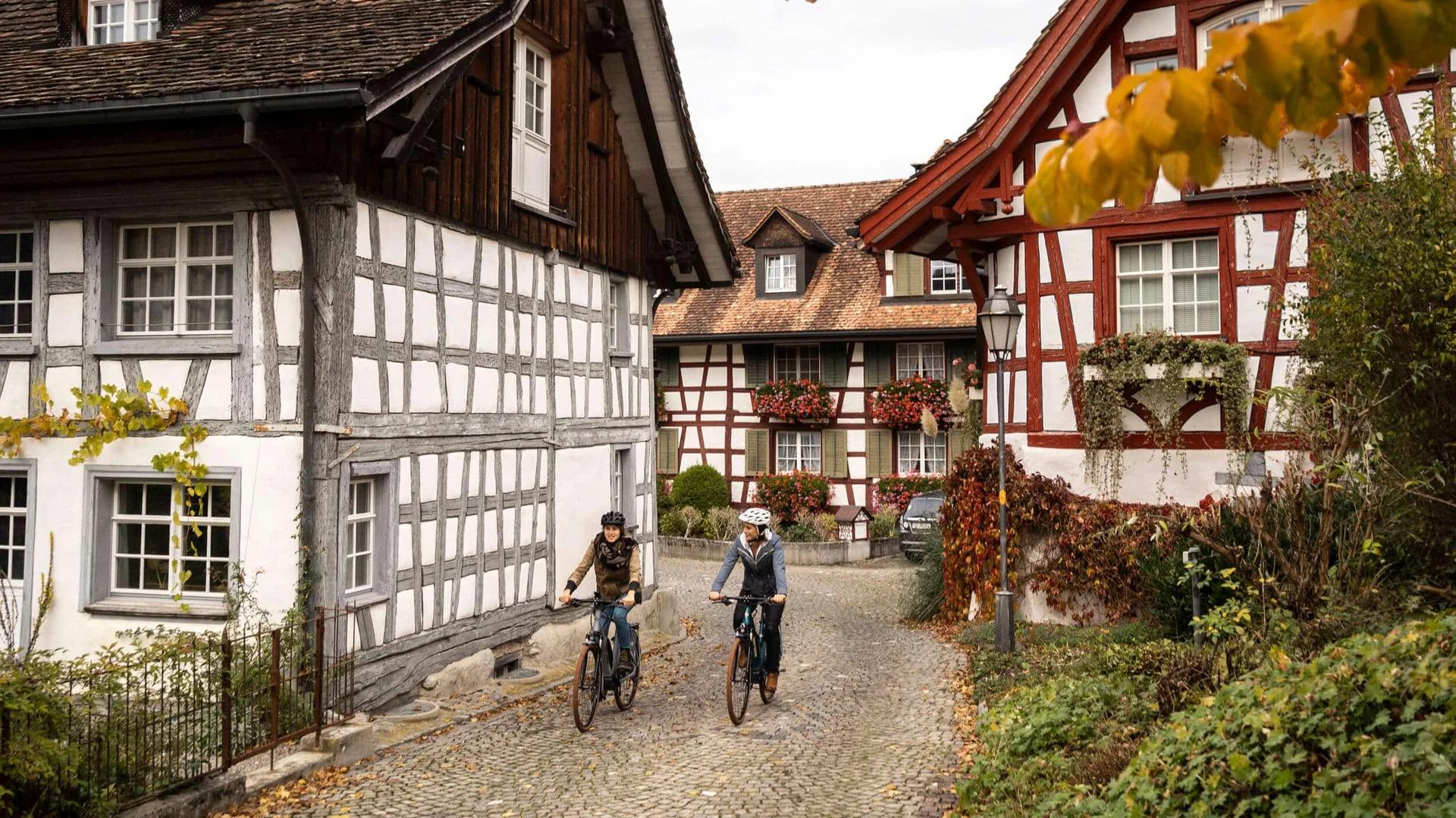Twee fietsers rijden door een historisch vakwerkdorp in de herfst
