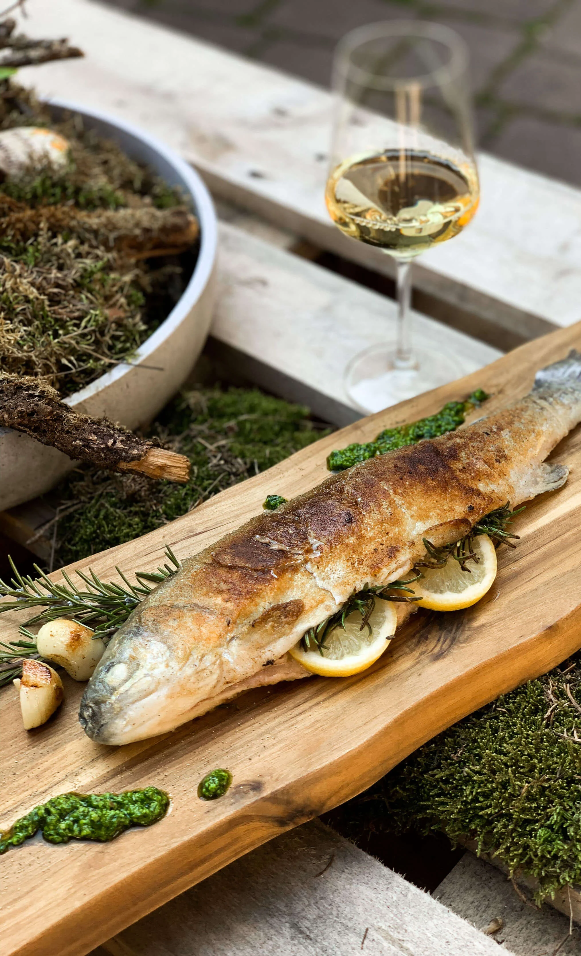 Gegrilde vis op houten plank met citroenschijfjes en glas witte wijn