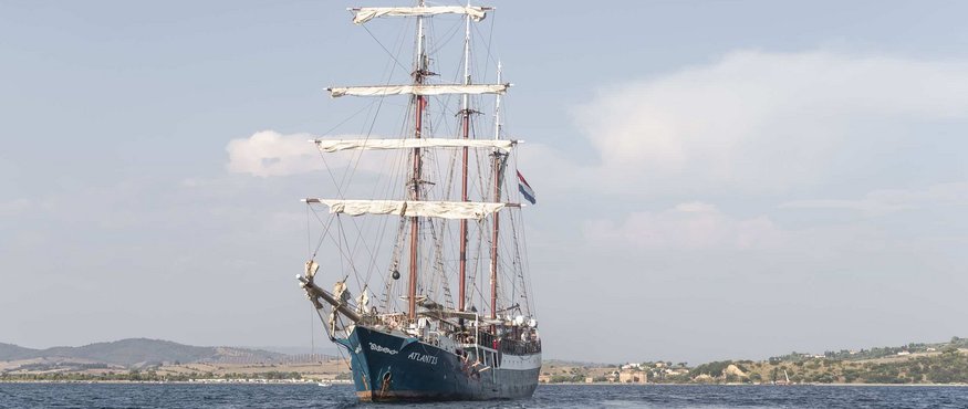 Sailing ship Atlantis on calm sea with coastal landscape