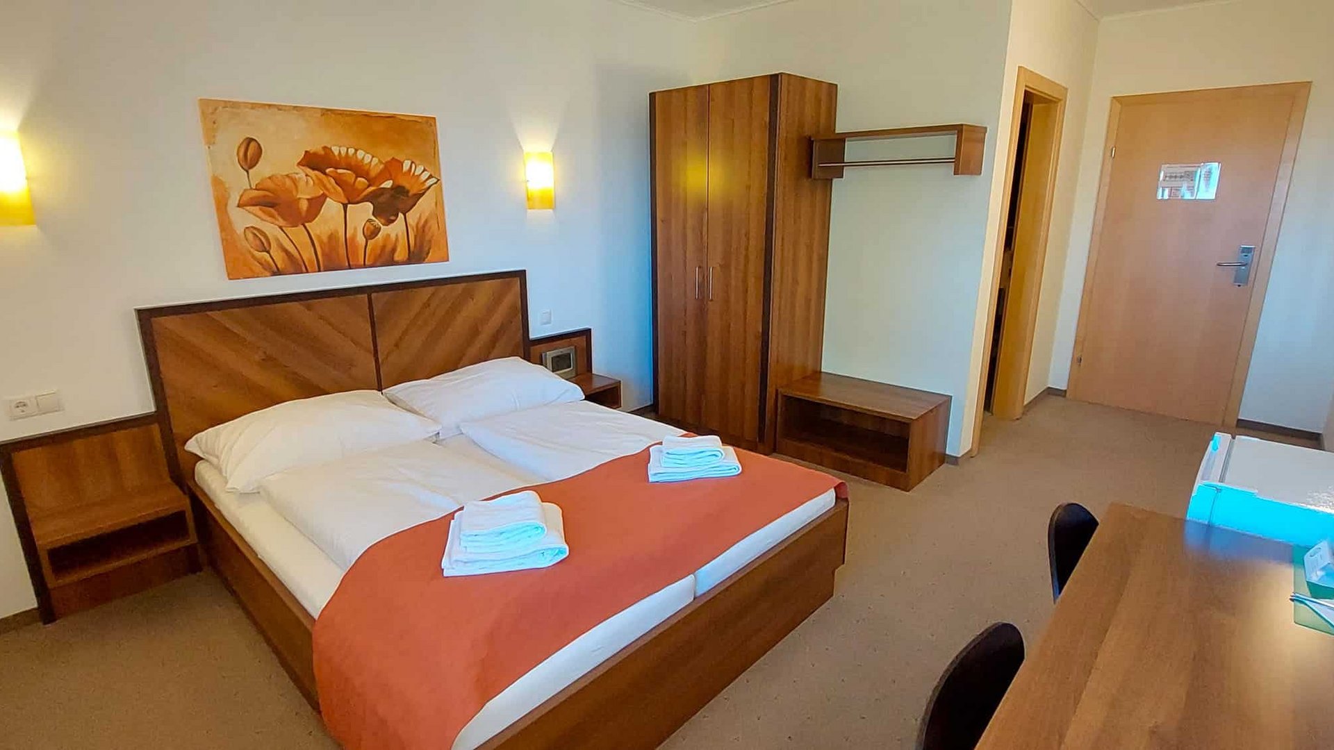 Small hotel room with double bed, wardrobe, and desk
