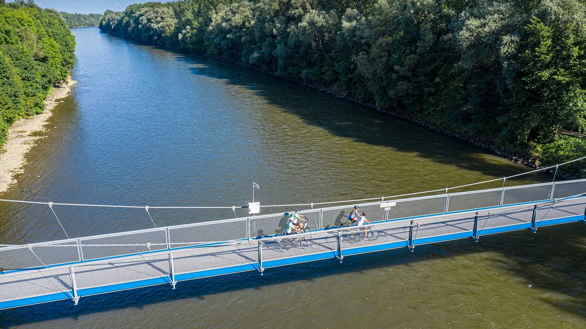 Fietsers op een blauwe voetgangersbrug over een rivier