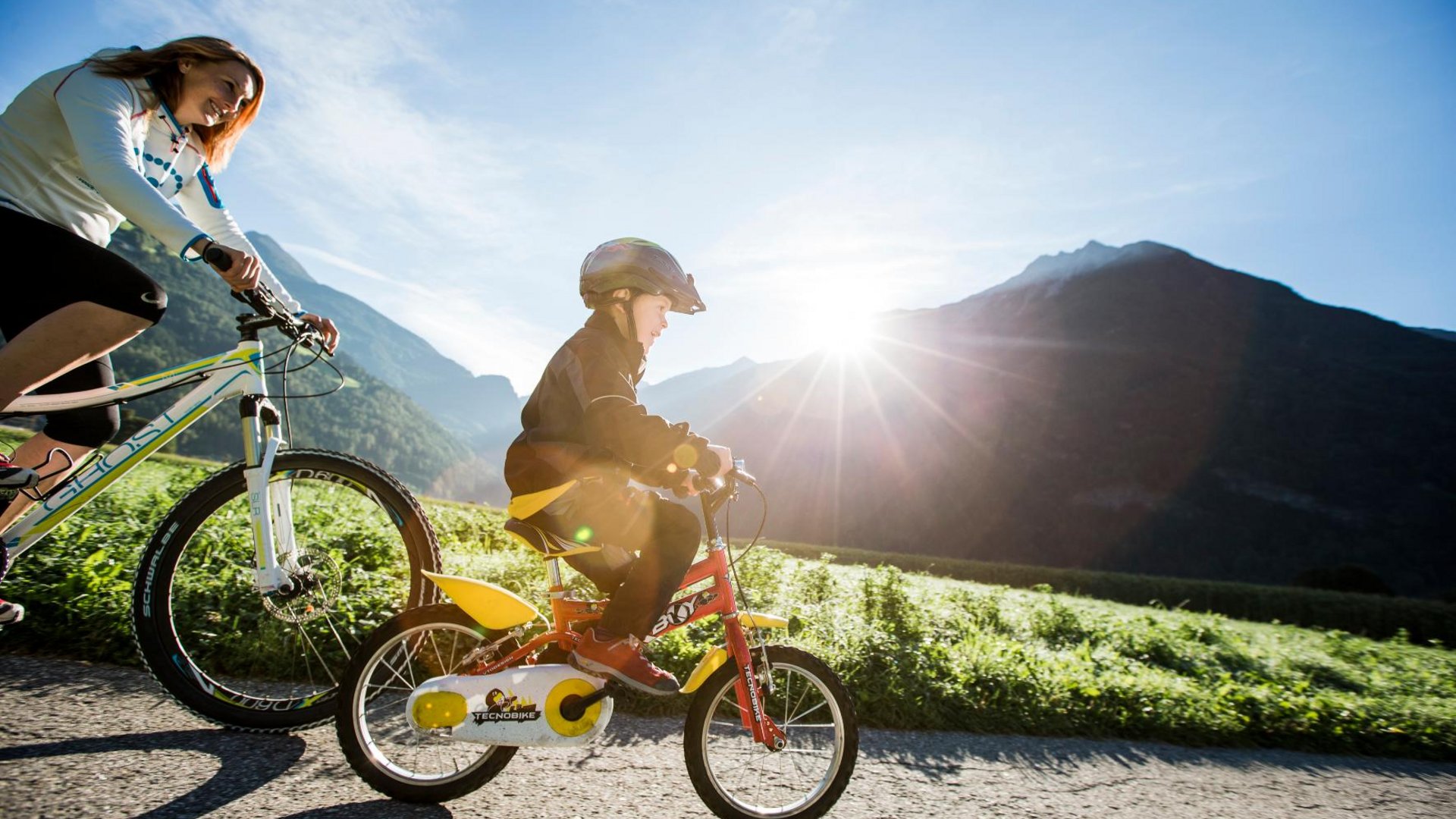 Woman and child cycling on a path in sunny mountain landscape