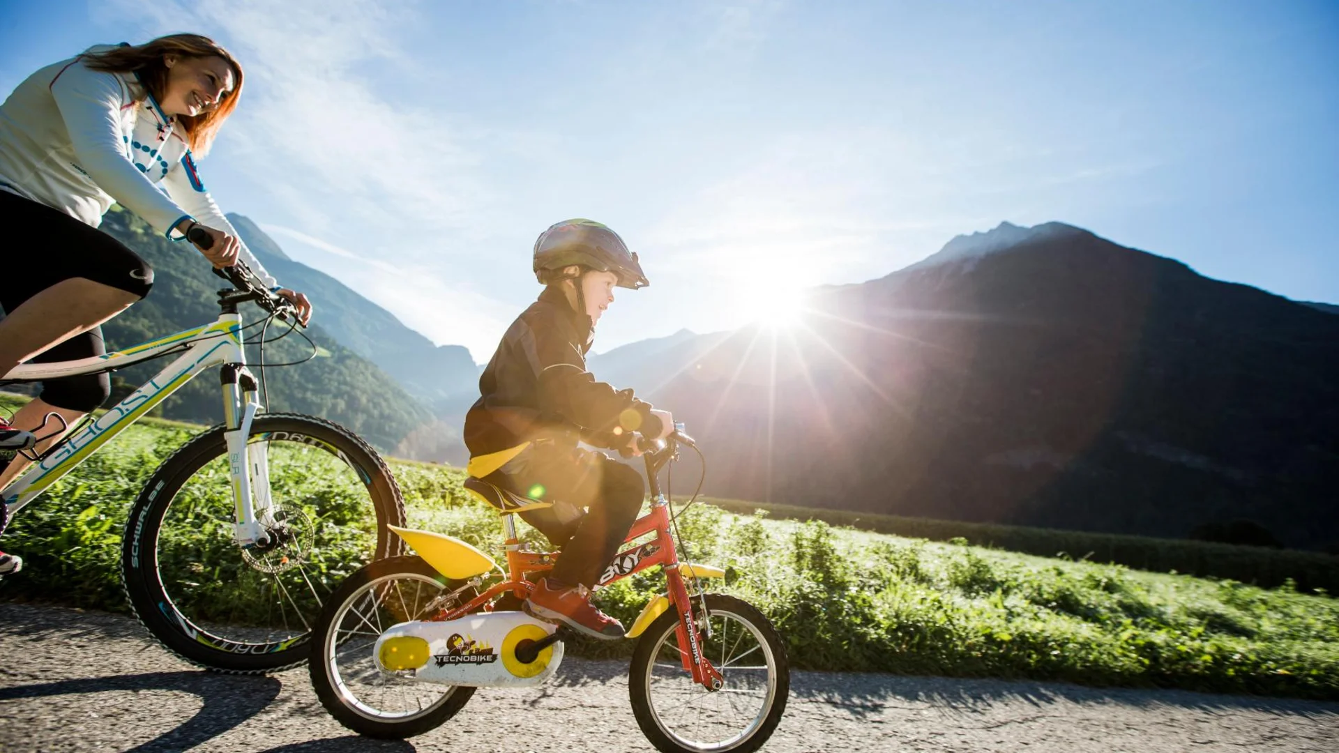Vrouw en kind fietsen op een pad bij zonnig berglandschap