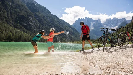Radreisen in der Gruppe © Velontour Drei Radfahrer spielen am Berghang am See mit Wasser an einem sonnigen Tag