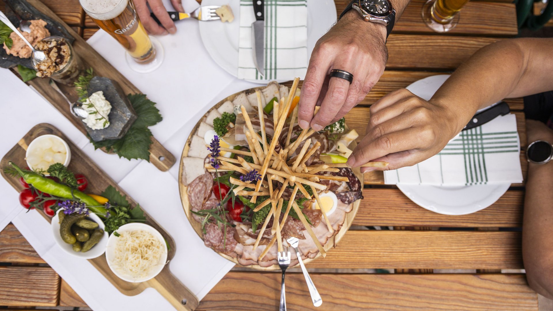 People reaching for breadsticks and charcuterie on rustic wooden table