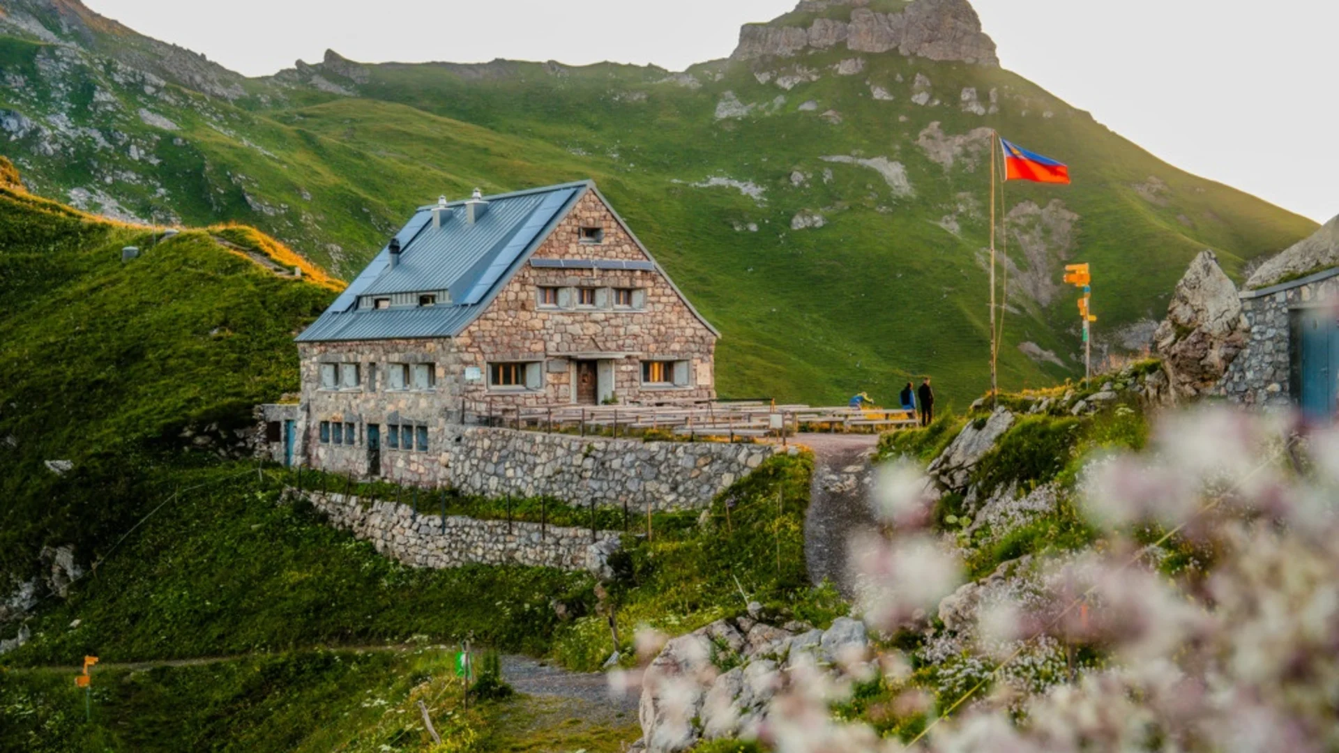 Steinernes Berghaus an einem grünen Berghang bei Sonnenuntergang