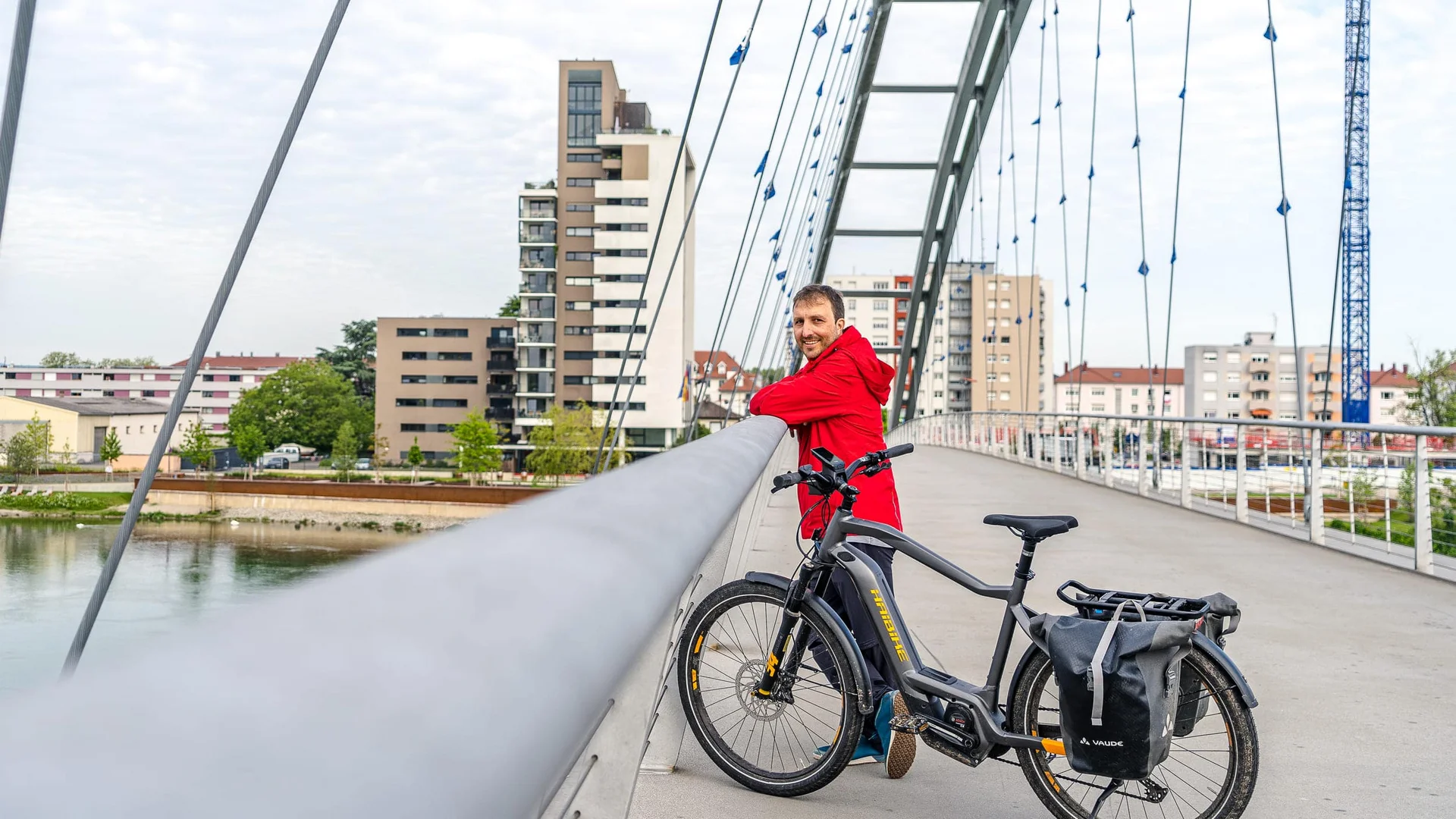 Man in rode jas met e-bike op moderne brug in de stad