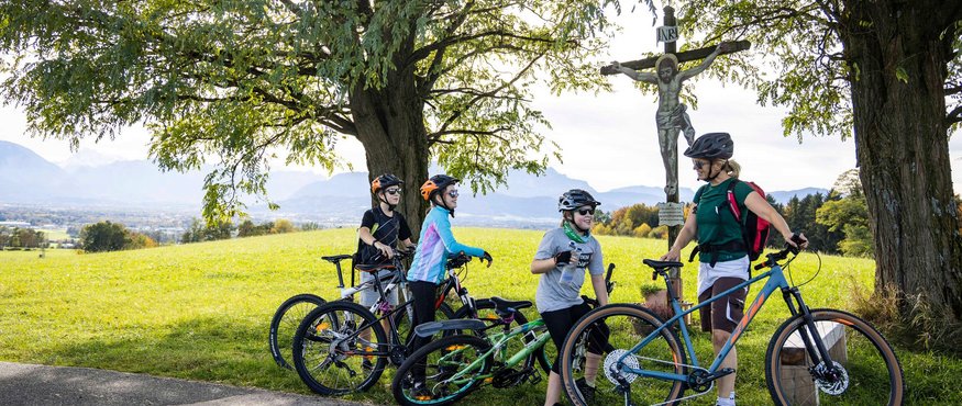 Familie mit Fahrrädern macht Pause unter Bäumen neben einem Kreuz
