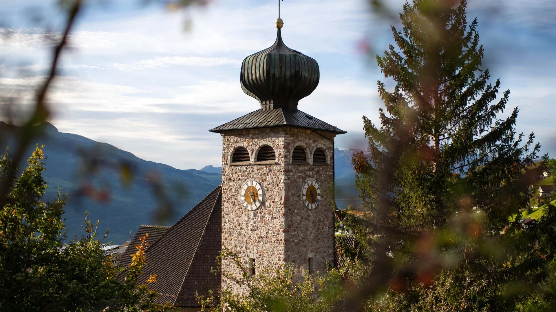 Kirchturm aus Stein mit Zwiebeldach in einer Berglandschaft
