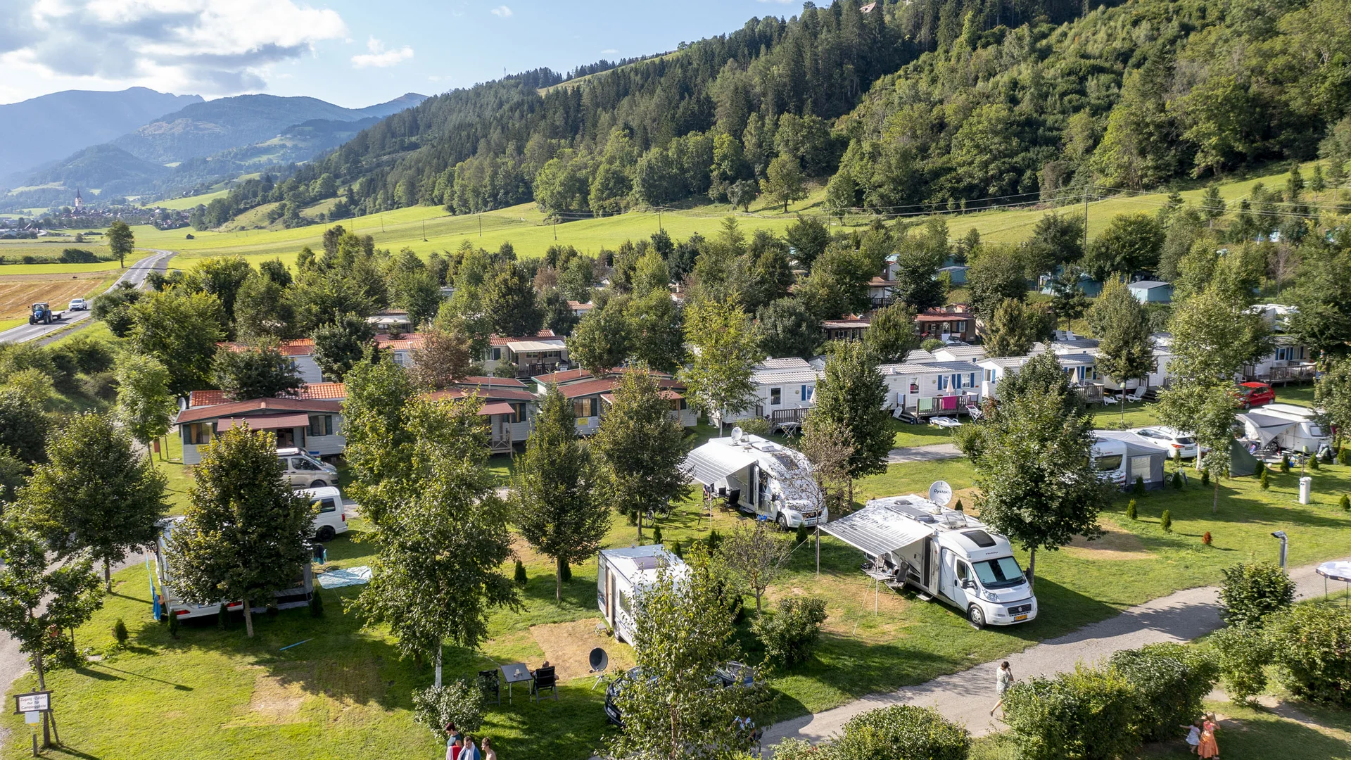 Campingplaats met campers en bomen bij bergen op een zonnige dag
