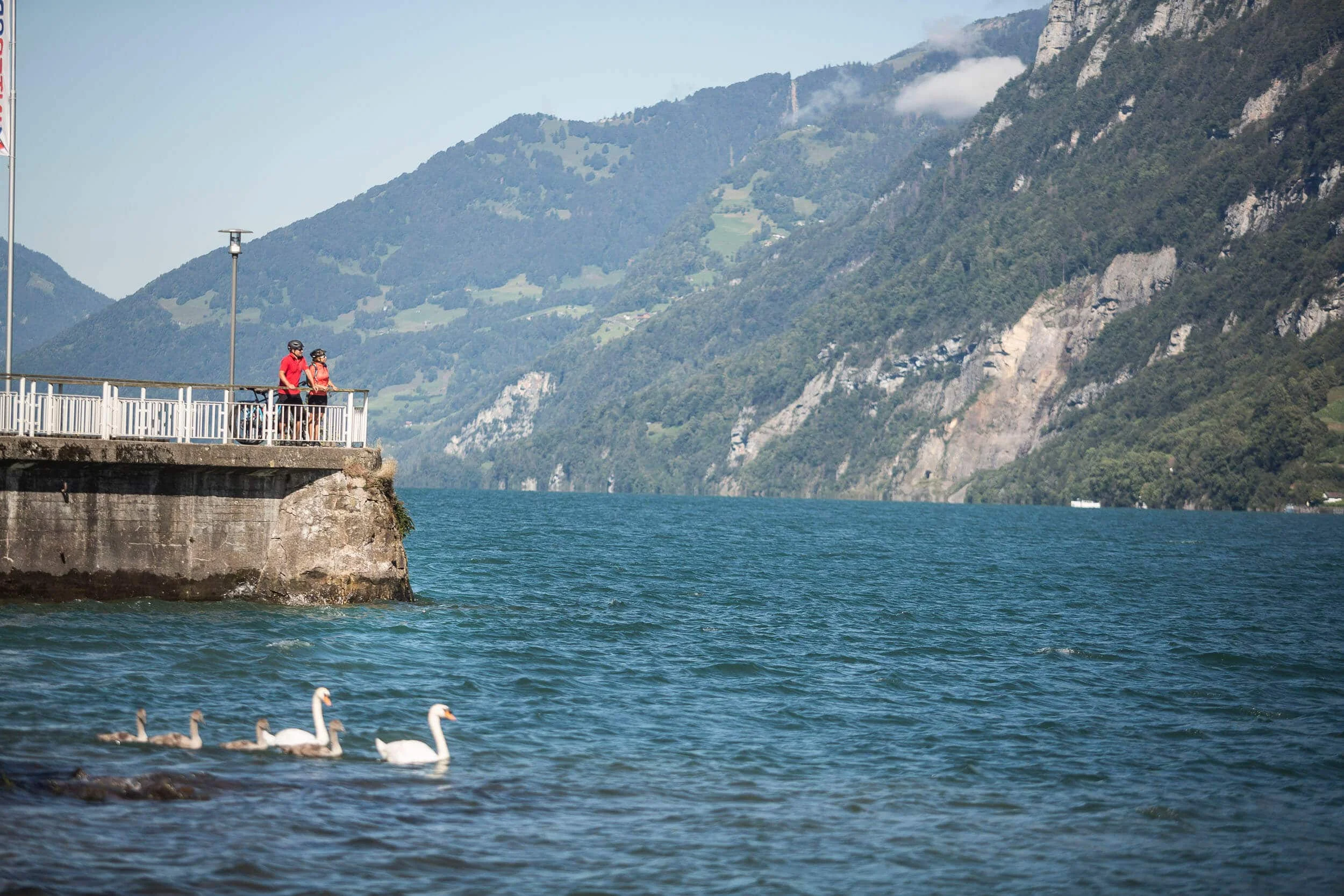 Zwitserland Twee fietsers op een promenade langs het meer met zwanen en bergen op de achtergrond