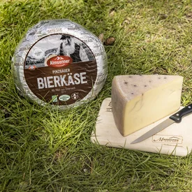 Pinzgauer Bierkäse op houten plank met mes op gras