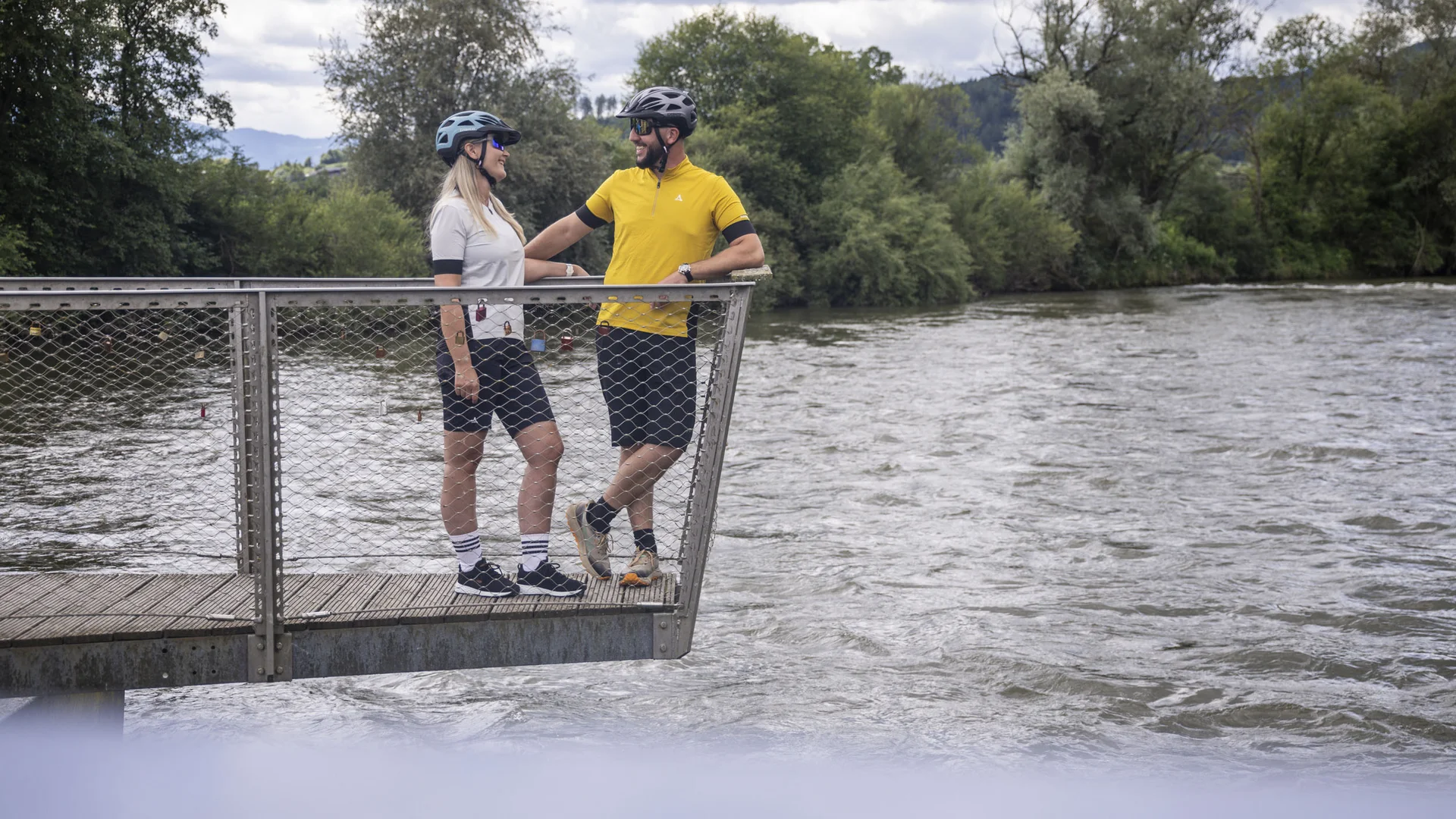 Twee fietsers met helmen op een brug over een rivier