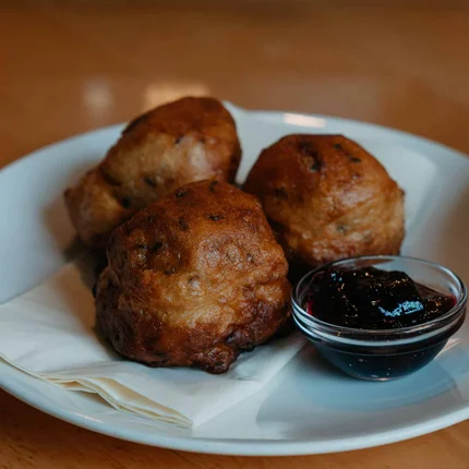 Drie gefrituurde deegballetjes met donkere saus op een wit bord