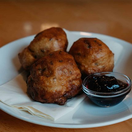 Three fried dough balls with dark sauce on a white plate