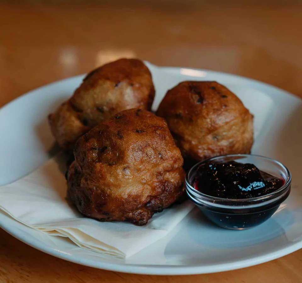 Drie gefrituurde deegballetjes met donkere saus op een wit bord