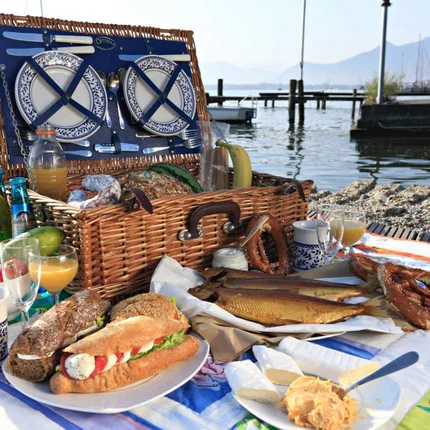 Picknickmand met brood, worst, pretzels, vis en drankjes aan het meer