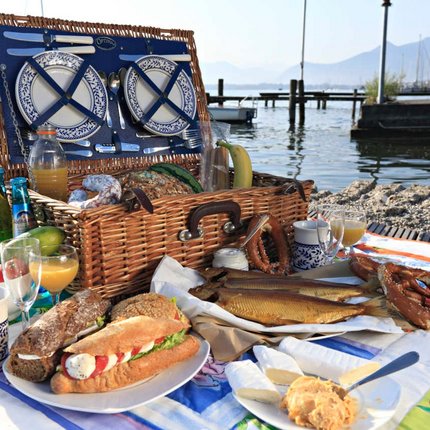 Picnic basket with bread, sausage, pretzels, fish, and drinks by the lake