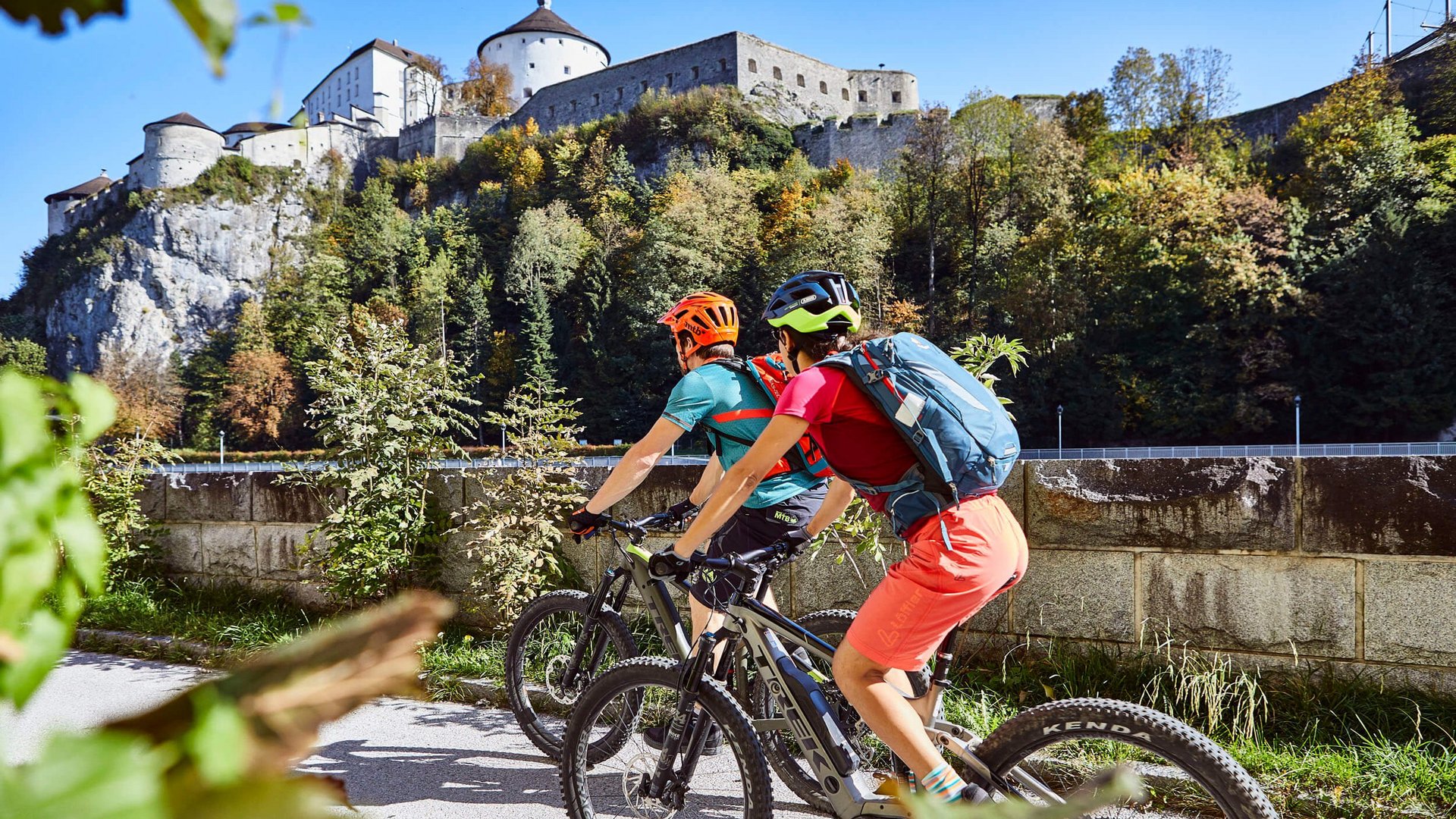 Two cyclists riding near a large castle on a sunny day