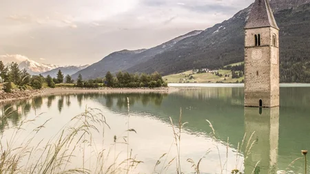 Ein Genuss-Radtag am Reschensee © IDM Südtirol - Marion Lafogler Unterwasserkirchturm im Reschensee vor Bergkulisse und Gras im Vordergrund