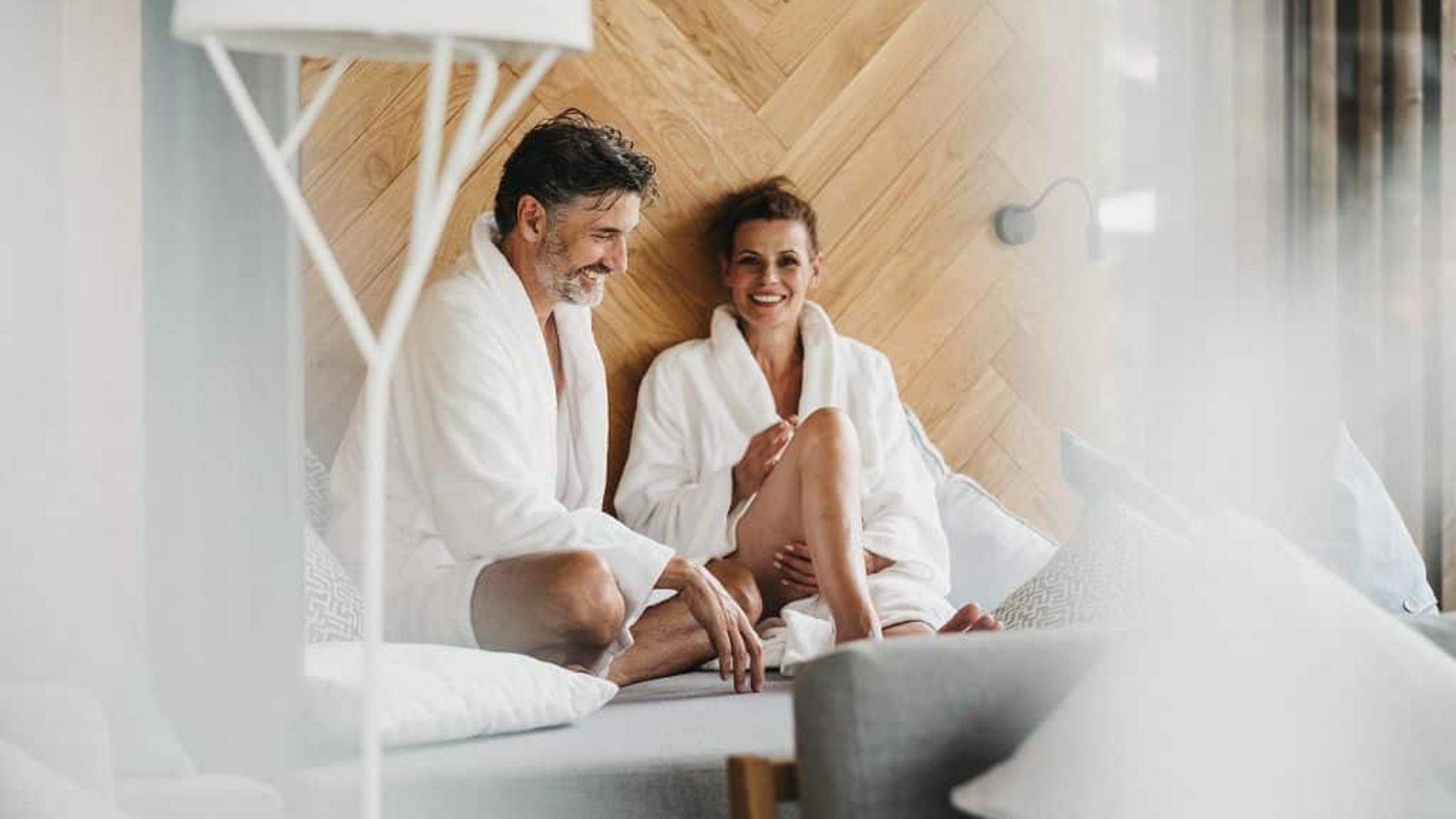 Couple in white bathrobes relaxing on couch with wooden wall background