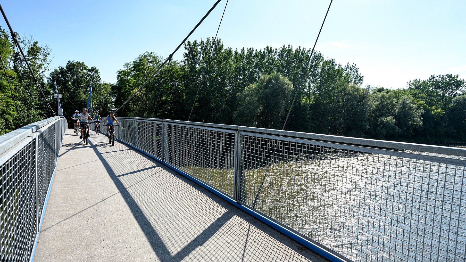 Cyclists riding on a suspension bridge over water on a sunny day