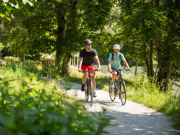 Kulinarisch Radeln rund um den Chiemsee © Velontour Zwei Radfahrer fahren auf einem Waldweg bei sonnigem Wetter