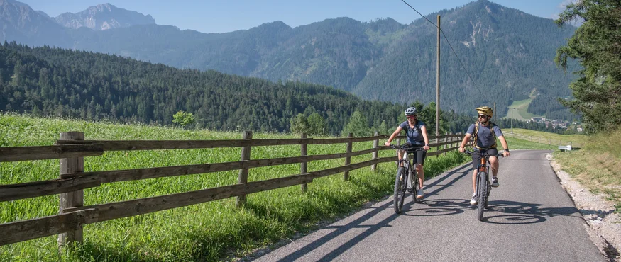 Twee fietsers op bergweg met houten hek en bos op de achtergrond