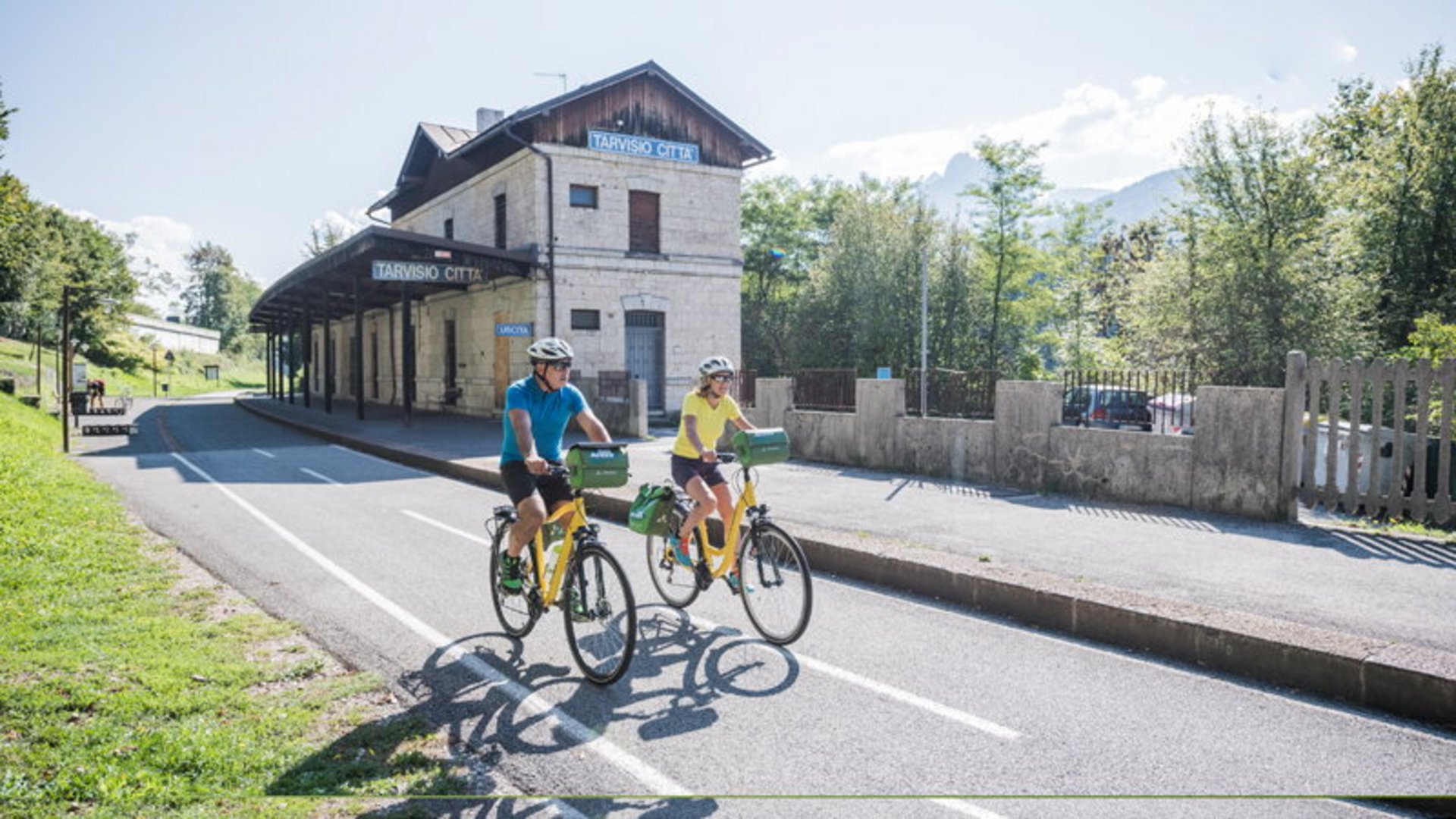Two cyclists riding past an old train station building