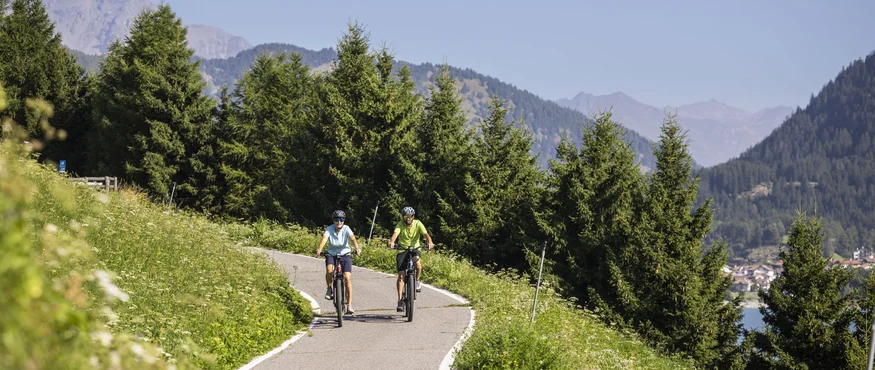 Drei Länder, du und dein Rad: Den Reschensee grenzüberschreitend entdecken © Heiko Mandl Zwei Radfahrer auf einem Bergweg mit Tannenbäumen und Bergen im Hintergrund