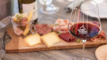Rotweinglas vor einer Platte mit Käse und Wurst auf Holztisch
