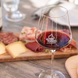 Glass of red wine with cheese and deli meat on wooden board