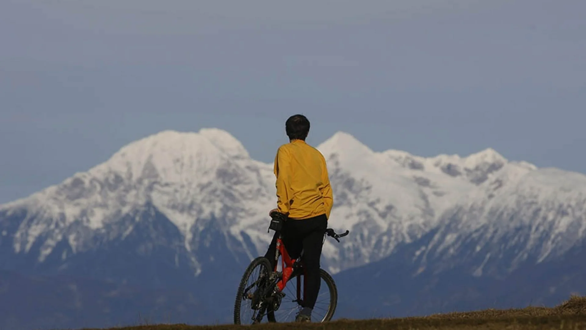 Persoon met fiets kijkt naar met sneeuw bedekte bergen