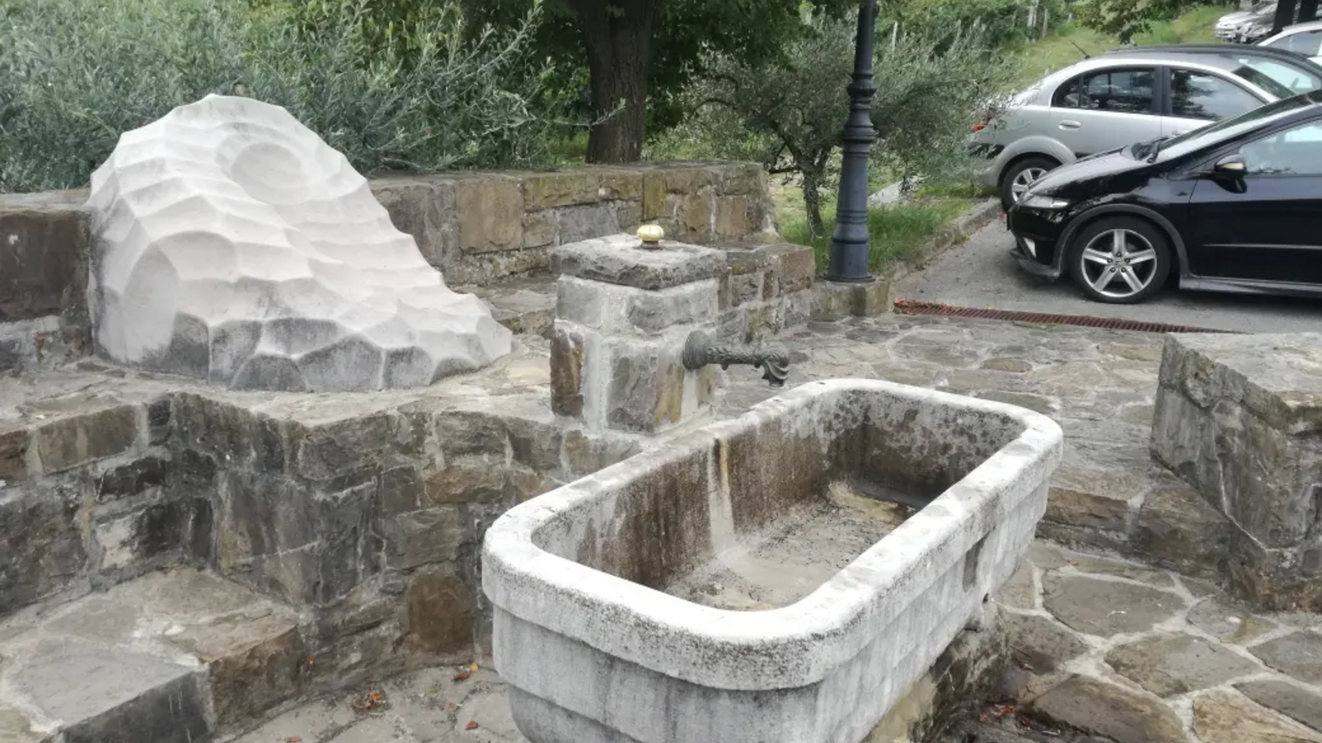 Stone fountain and seating area with parked cars in background