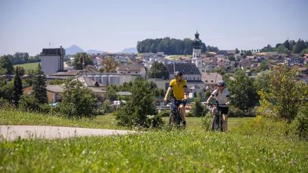Zwei Radfahrer fahren auf einem Weg mit Dorf und Kirche im Hintergrund
