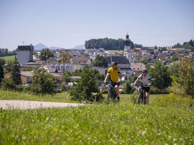 Zwei Radfahrer fahren auf einem Weg mit Dorf und Kirche im Hintergrund
