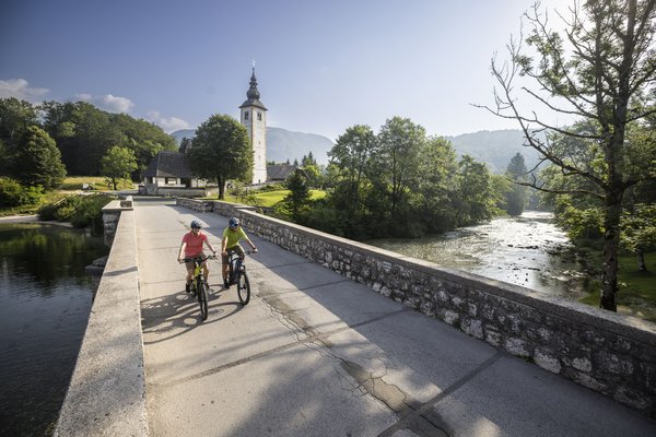 Cyclists on a bridge in rural area with church and river