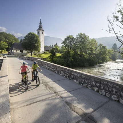Fietsers op brug in landelijke omgeving met kerk en rivier