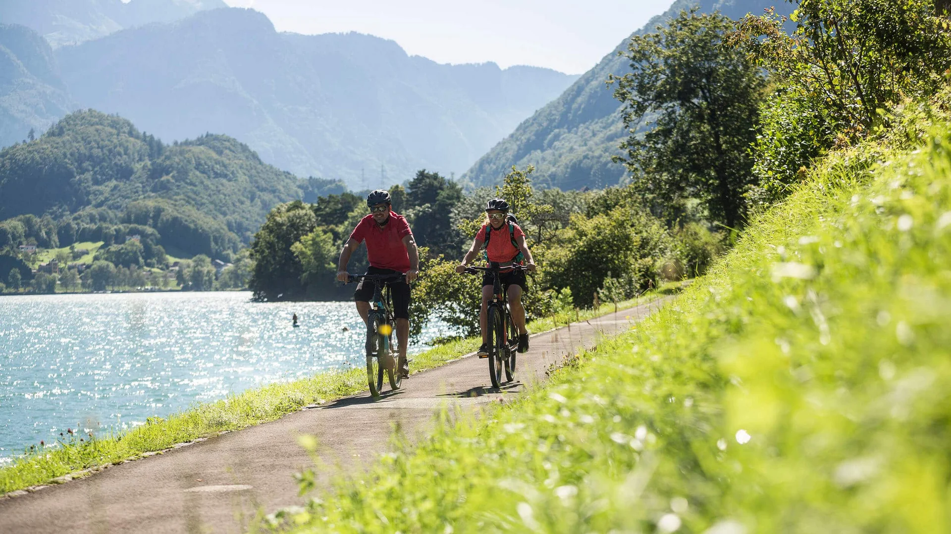 Twee fietsers op een pad langs het meer met bergen op de achtergrond