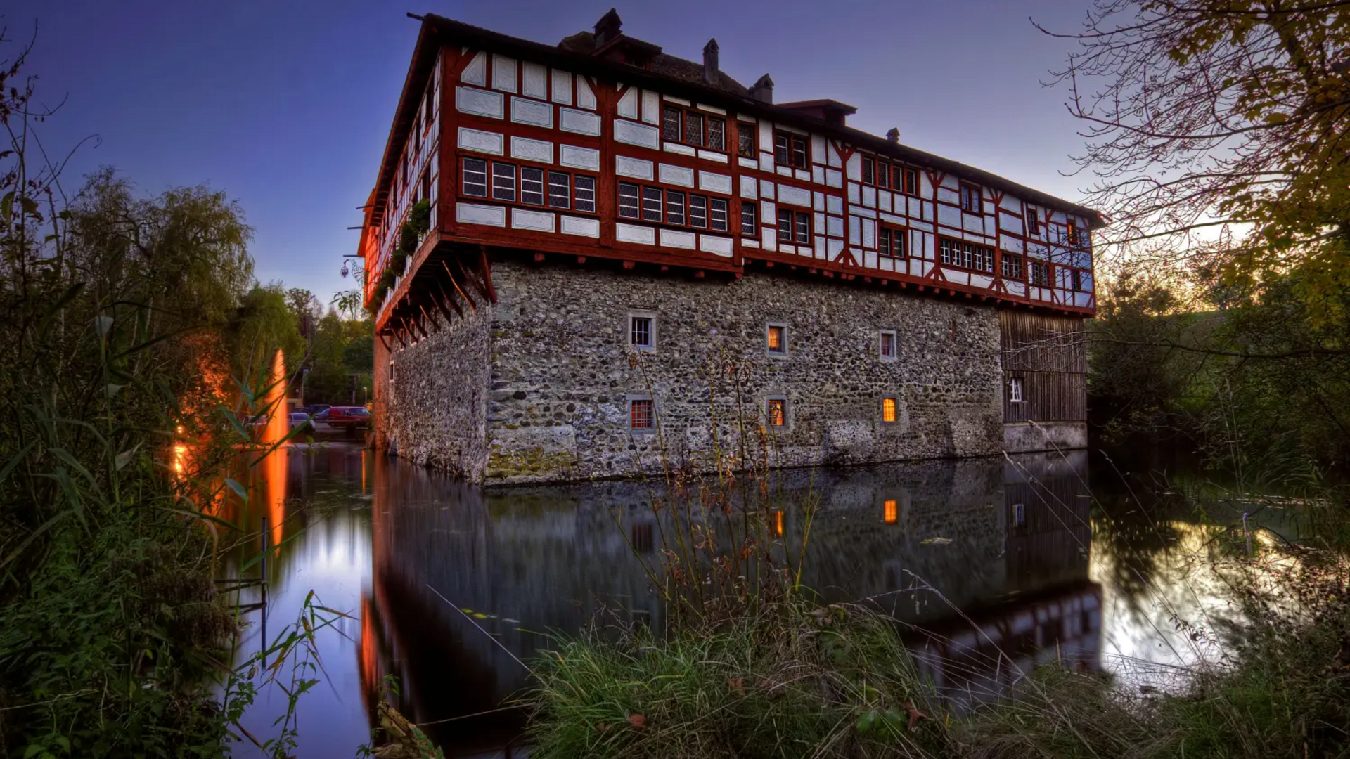 Historic half-timbered house on stone base over water at dusk