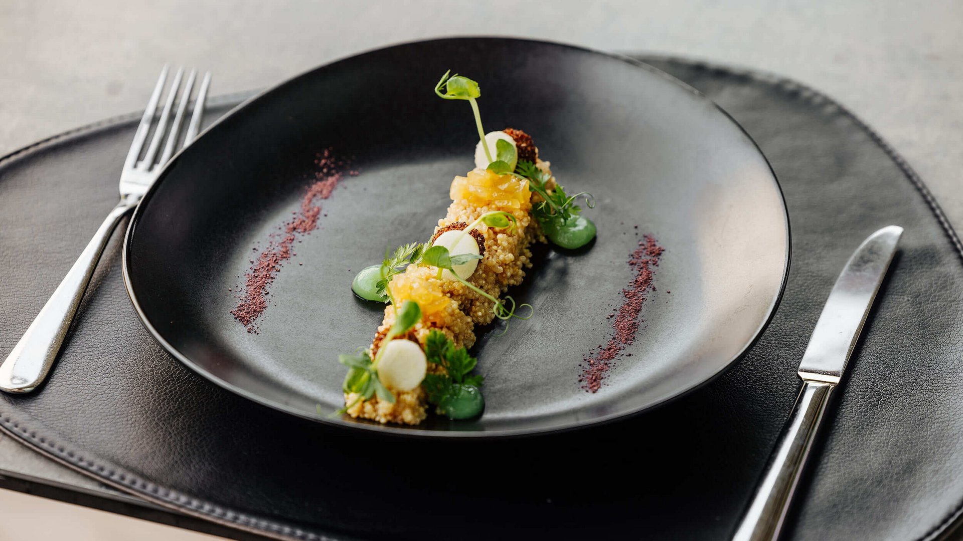 Artistically plated dish on a black plate with herbs and sauces.