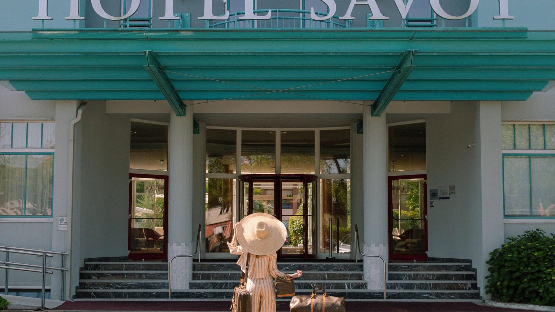 Woman with hat and luggage in front of Hotel Savoy entrance