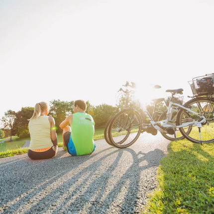 Two people sitting on a path next to their bicycles in sunlight