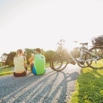 Zwei Personen sitzen auf einem Weg neben ihren Fahrrädern im Sonnenlicht