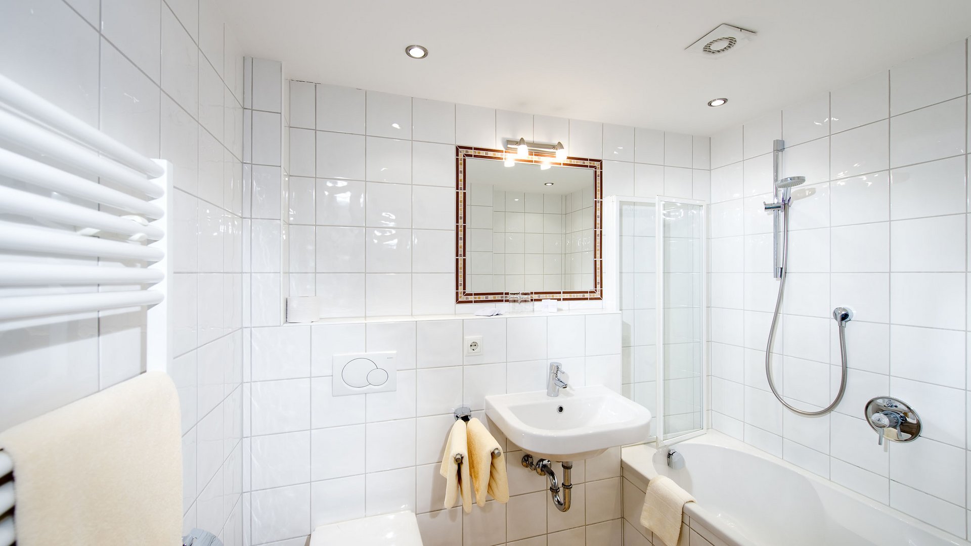 Modern white tiled bathroom with toilet, sink, and bathtub